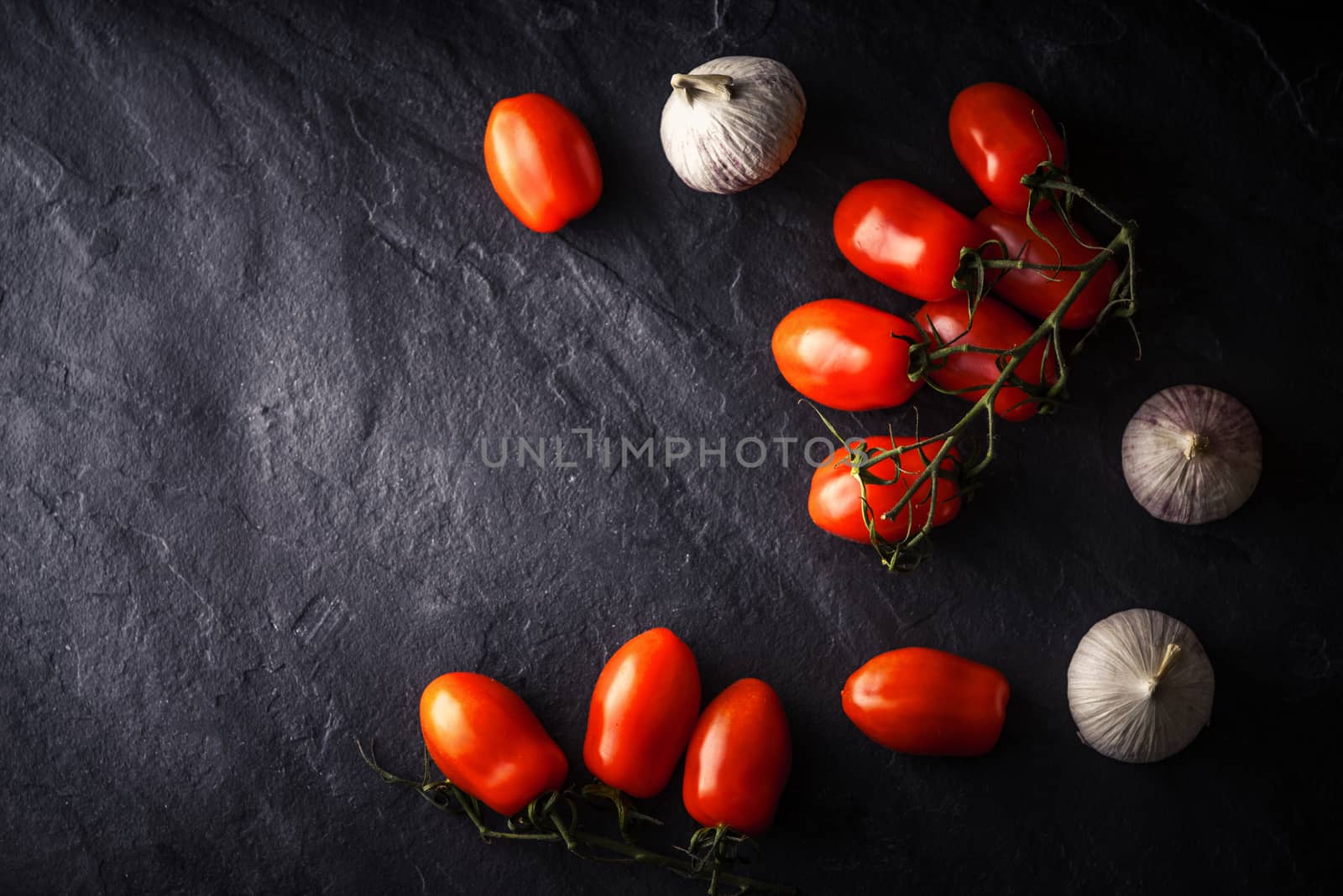 Cherry tomatoes with garlic on the black stone table by Deniskarpenkov