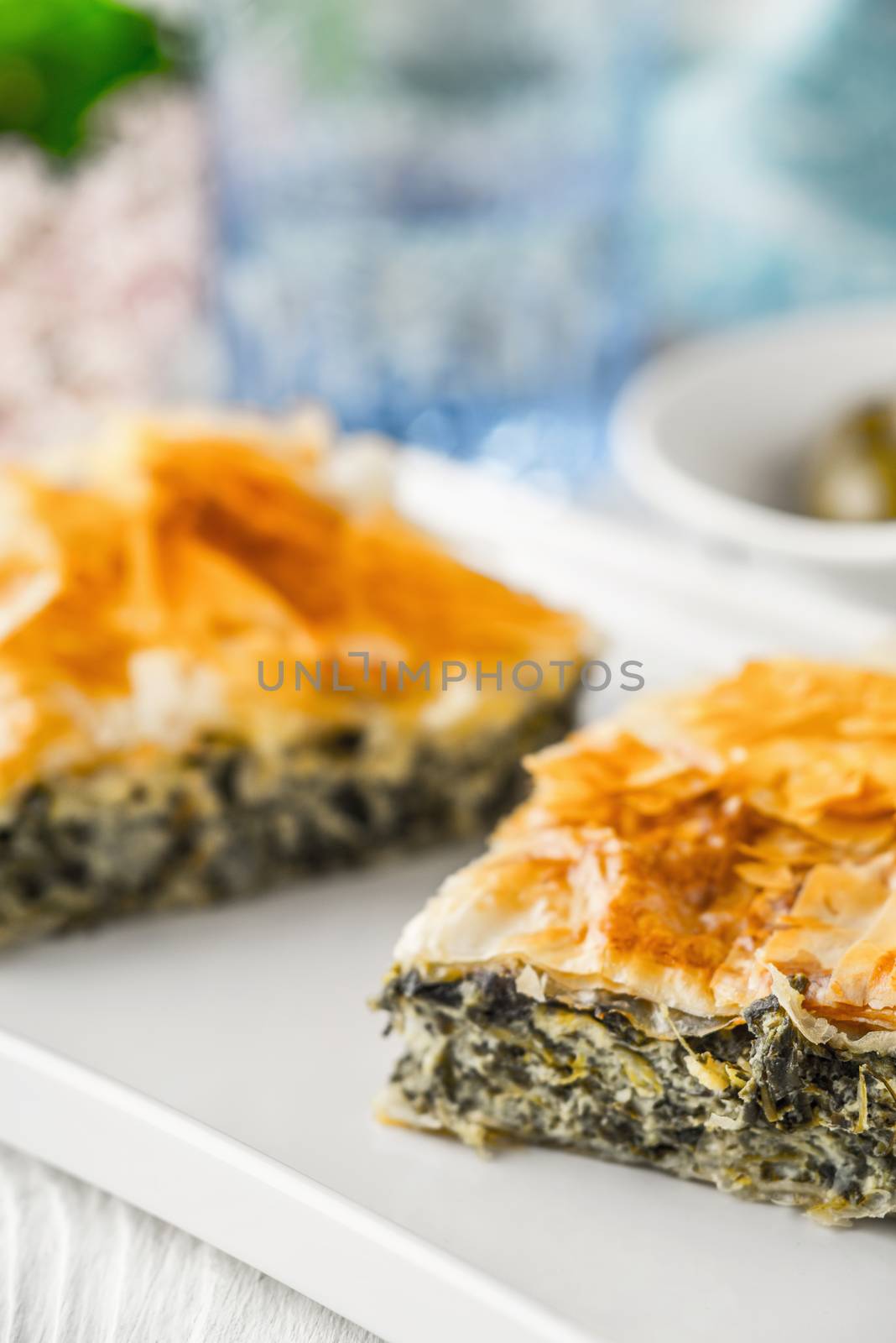 Greek pie spanakopita on the white plate with blurred accessorizes by Deniskarpenkov