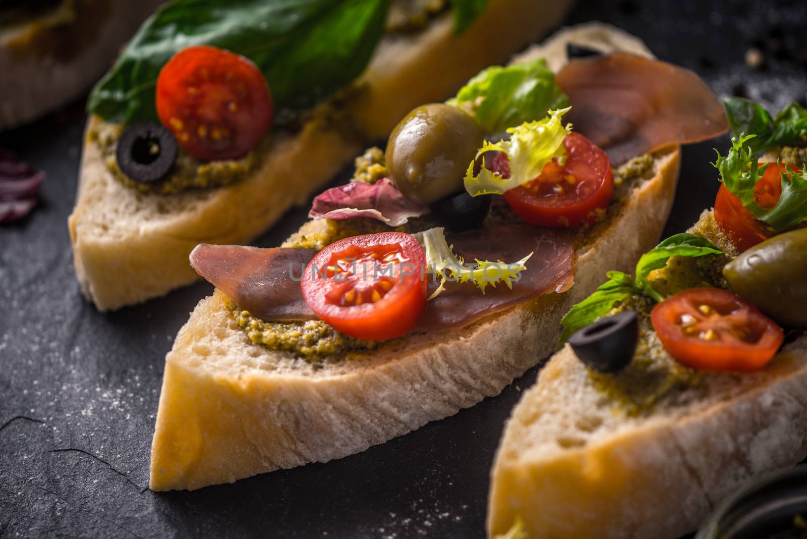 Slices of ciabatta with olives , tomatoes and basil on the black stone table horizontal