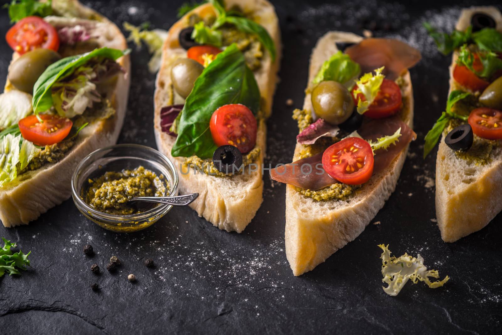 Slices of ciabatta with olives , tomatoes and basil on the black stone table by Deniskarpenkov