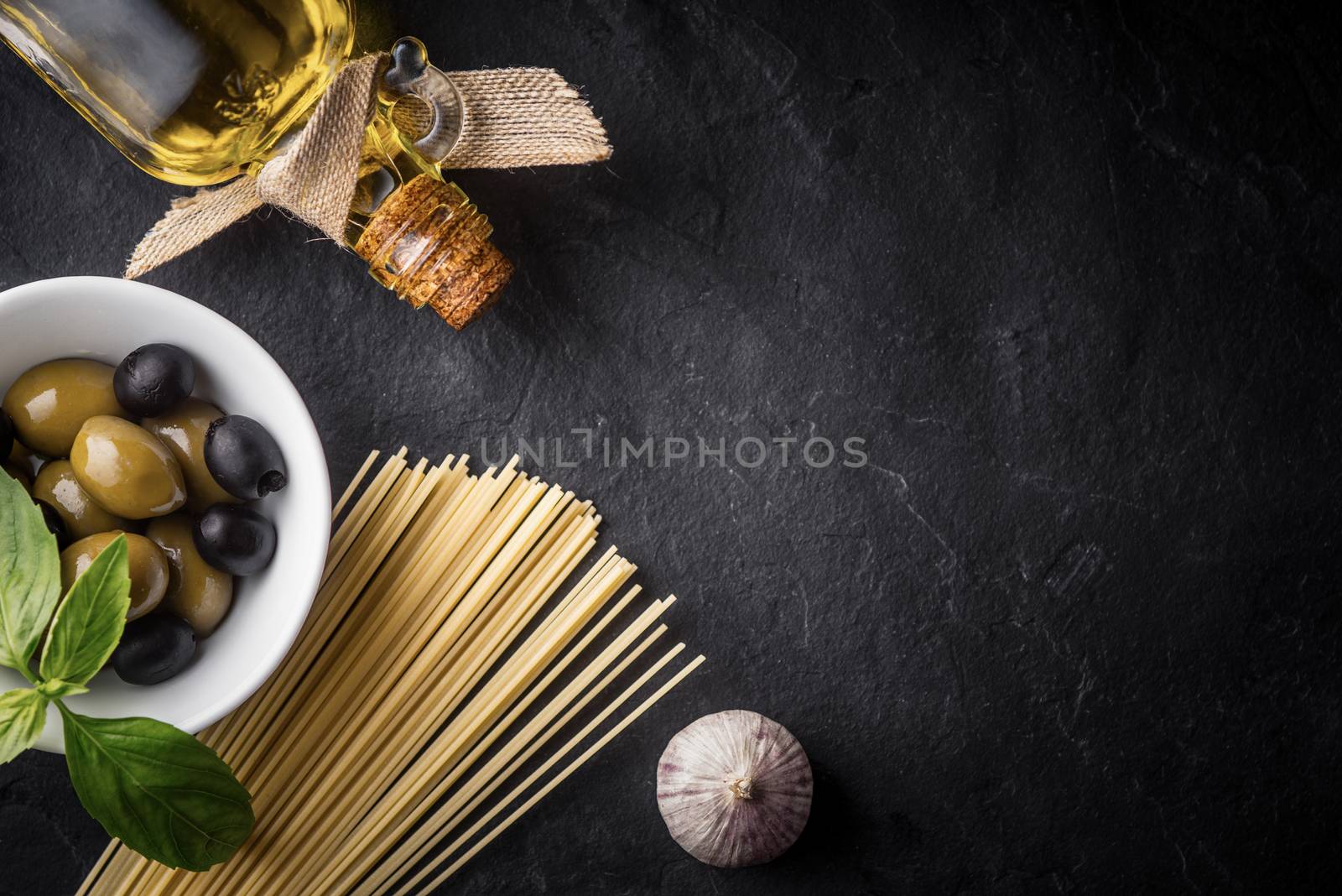 Spaghetti, olives and olive oil on the black stone table by Deniskarpenkov