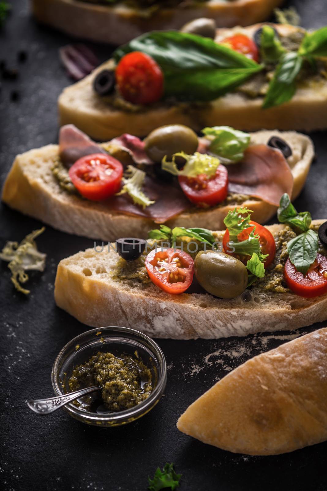 Slices of ciabatta with olives , tomatoes and basil on the black stone table vertical by Deniskarpenkov