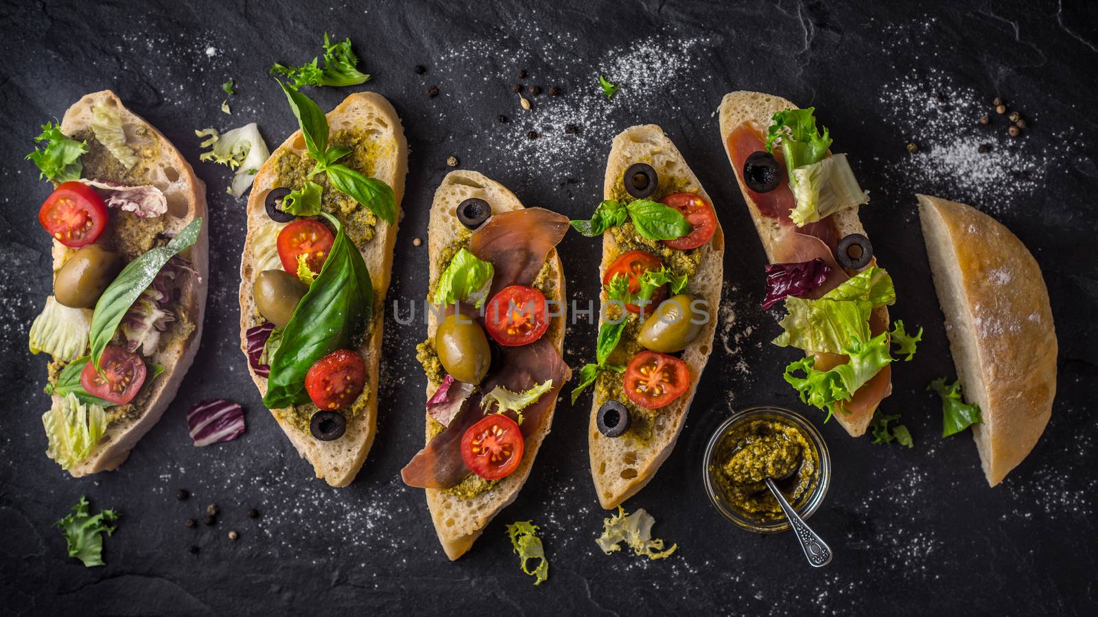 Slices of ciabatta with olives , tomatoes and basil on the black stone table wide screen