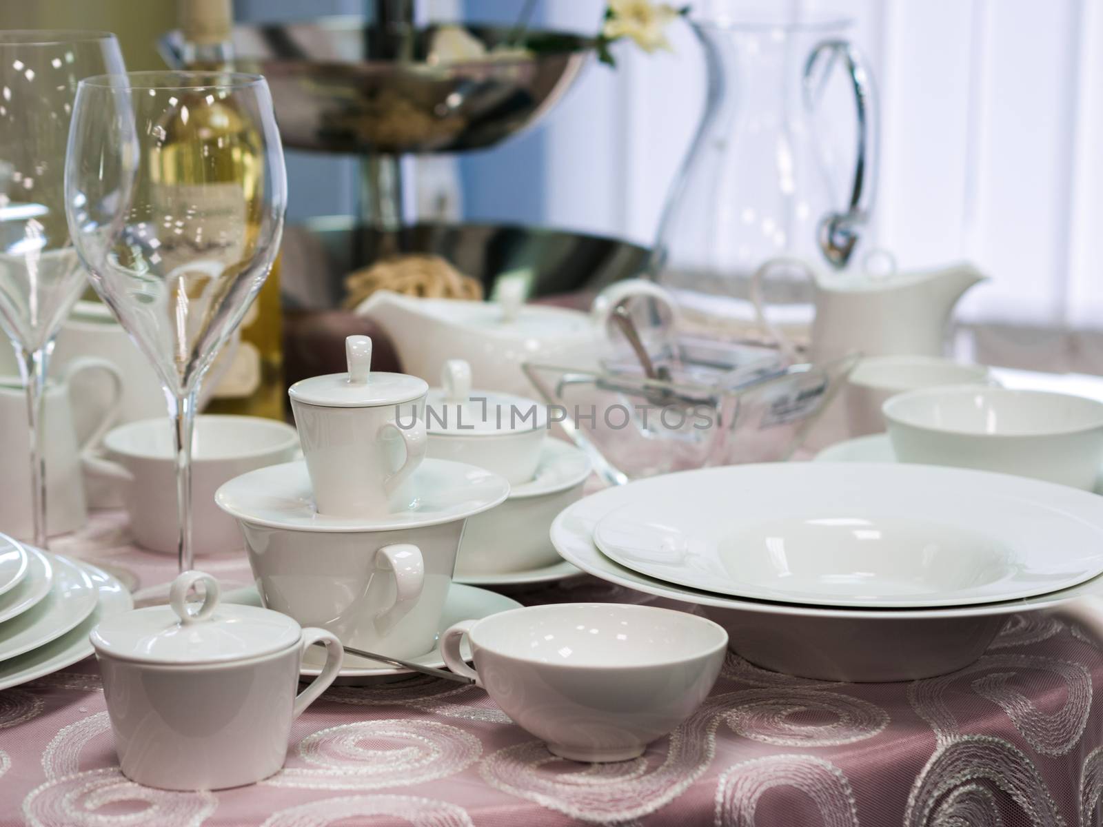 Set of new dishes on table with tablecloth. Stack of white plates and wine glasses on restaurant table. Shallow DOF