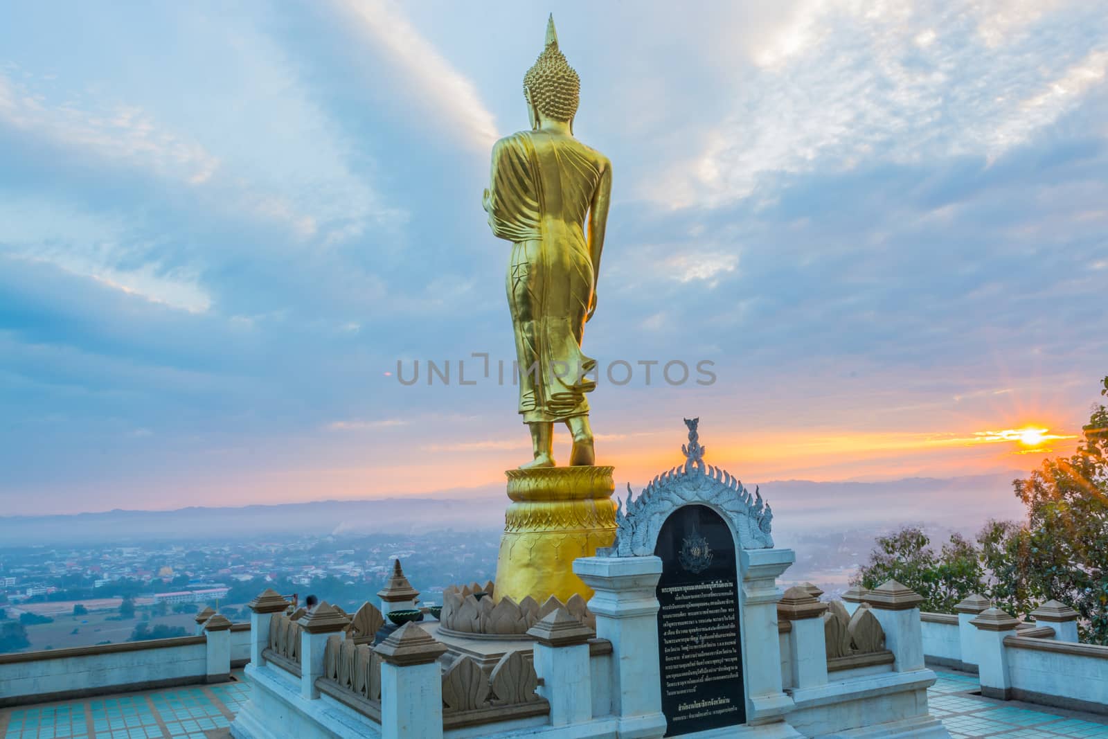 Buddha statue facing cityscape in morning sunrise on mountain top in Nan provincial town, Northern Thailand.