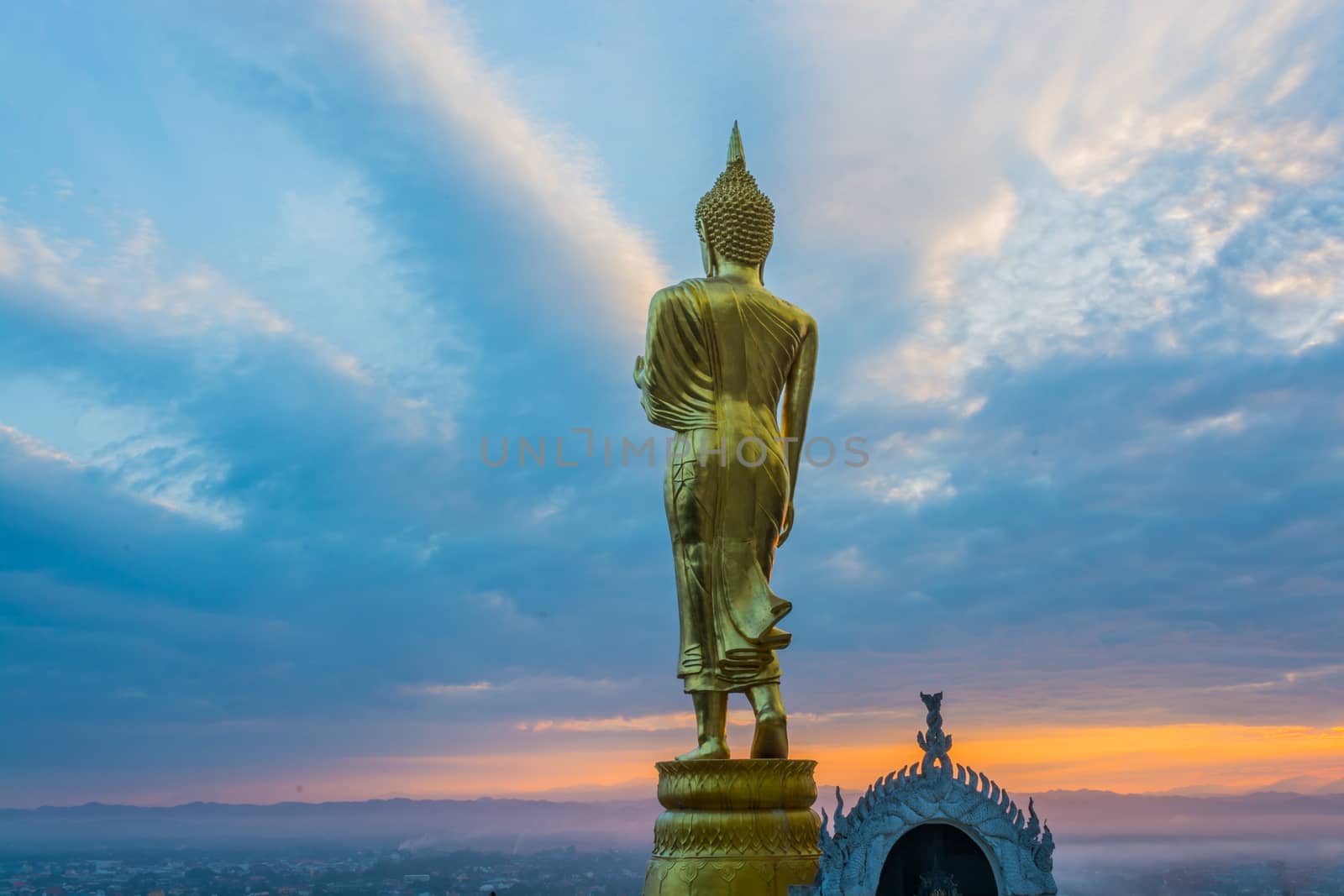 Buddha statue facing cityscape in morning sunrise on mountain top in Nan provincial town, Northern Thailand.