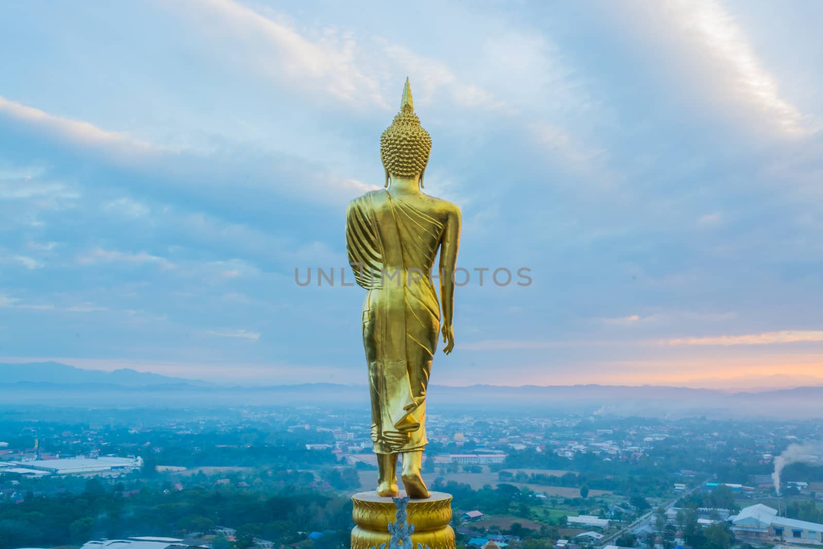 Buddha statue facing cityscape in morning sunrise on mountain top in Nan provincial town, Northern Thailand.