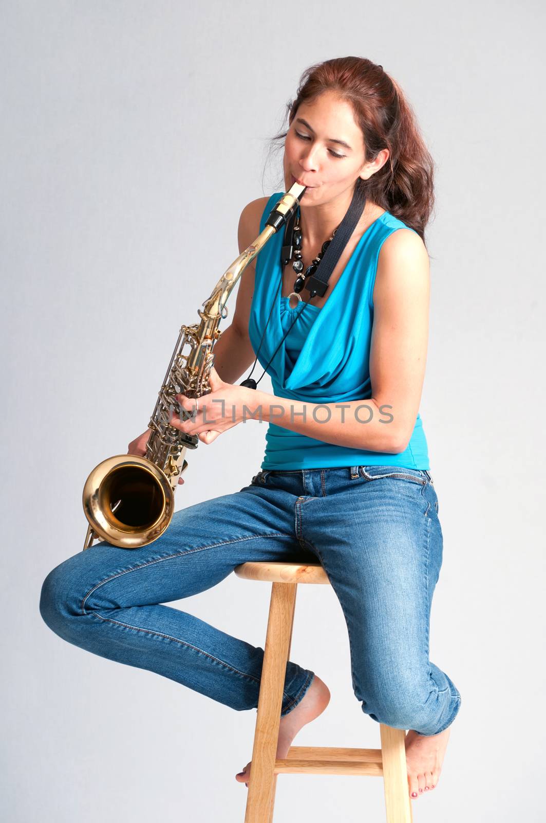 Pretty brunette girl practicing on the saxophone while seated barefooted on a stool
