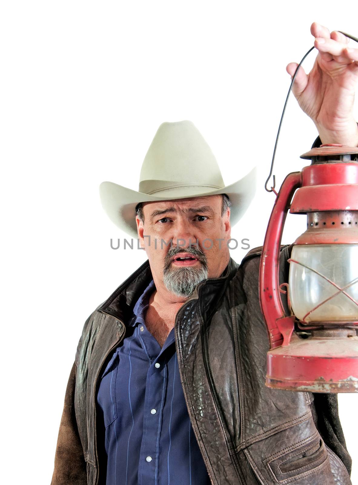 Mature cowboy looking forward by light of his handheld kerosene lantern. Isolated on a white background.