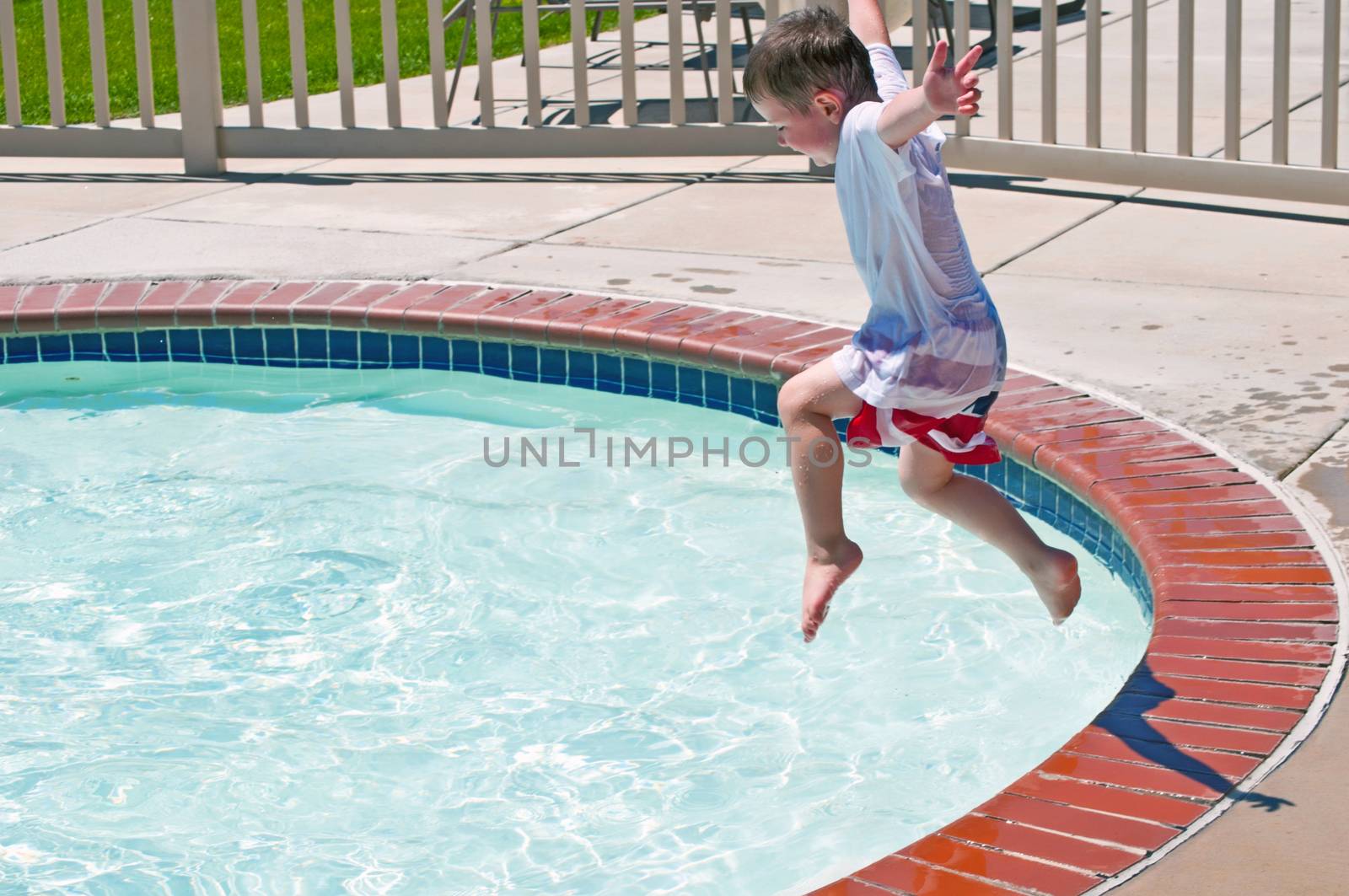 Exuberant little boy jumping into the water having fun at the local swimming pool.