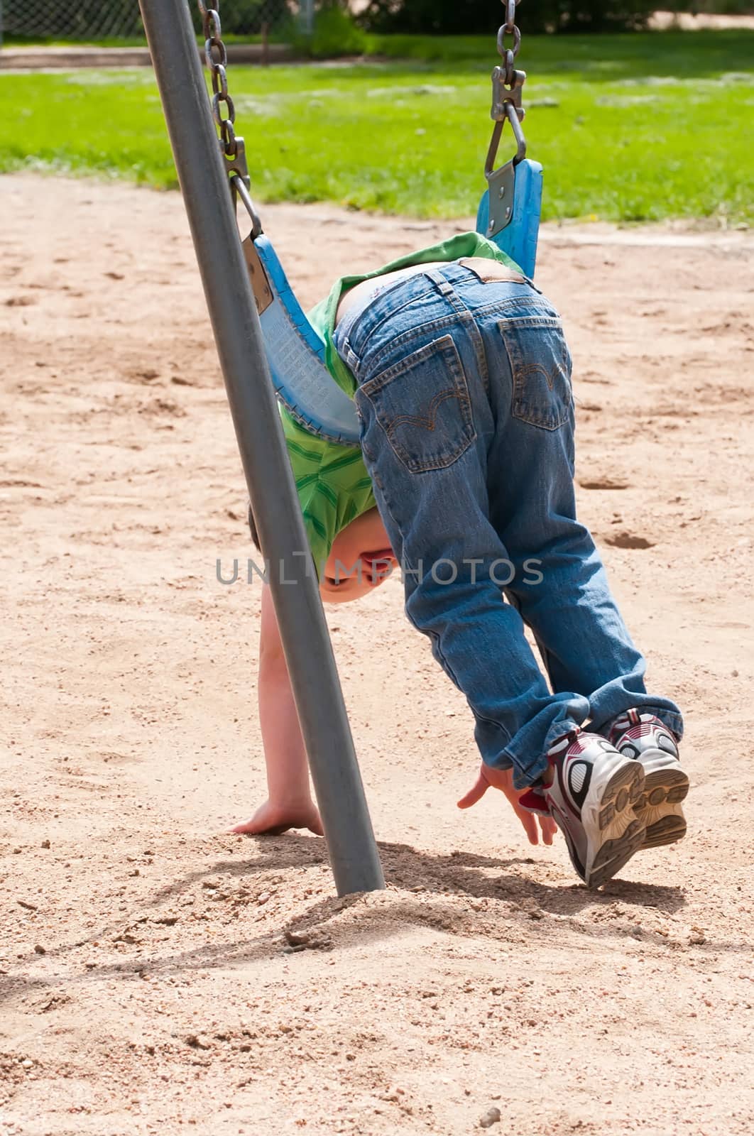 Cute little boy laying on his stomach in a swing while playing in the sand below.