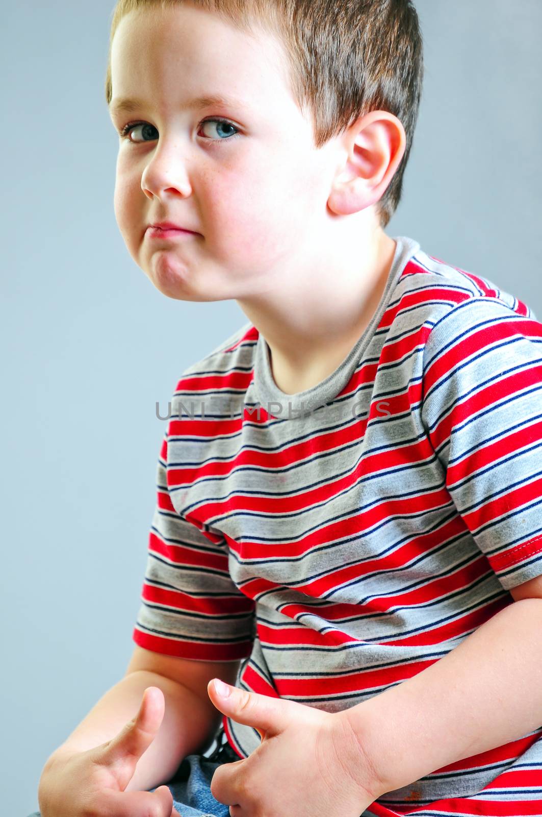 Cute little boy putting on his best tough guy look against a grey background.