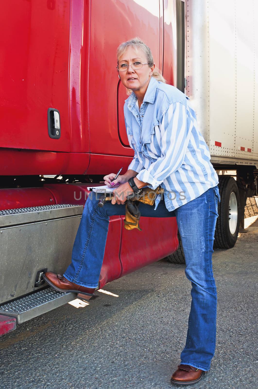 Pretty adult blonde woman doing a pre-trip inspection on her big truck before starting the delivery run.