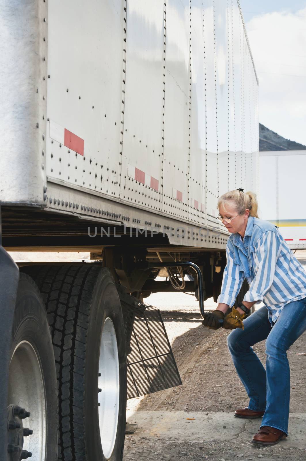 Pretty blonde woman truck driver cranking the dolly handle to raise the legs of a traier after backing her tractor under it.