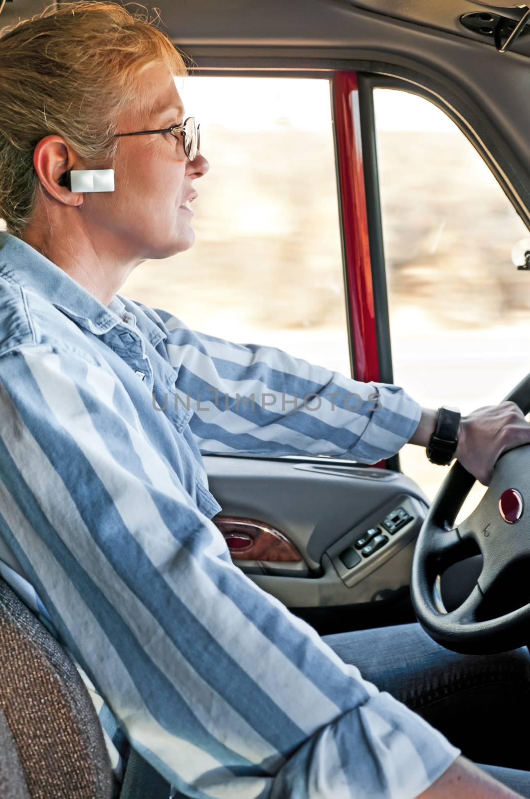 Pretty adult woman truck driver talking on her hands-free bluetooth device connected to her cellphone.