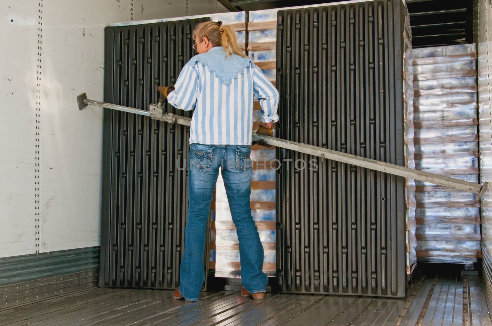 Pretty blonde woman placing a load-lock in the inside of a trailer to secure the loaded pallets during the upcoming trip.