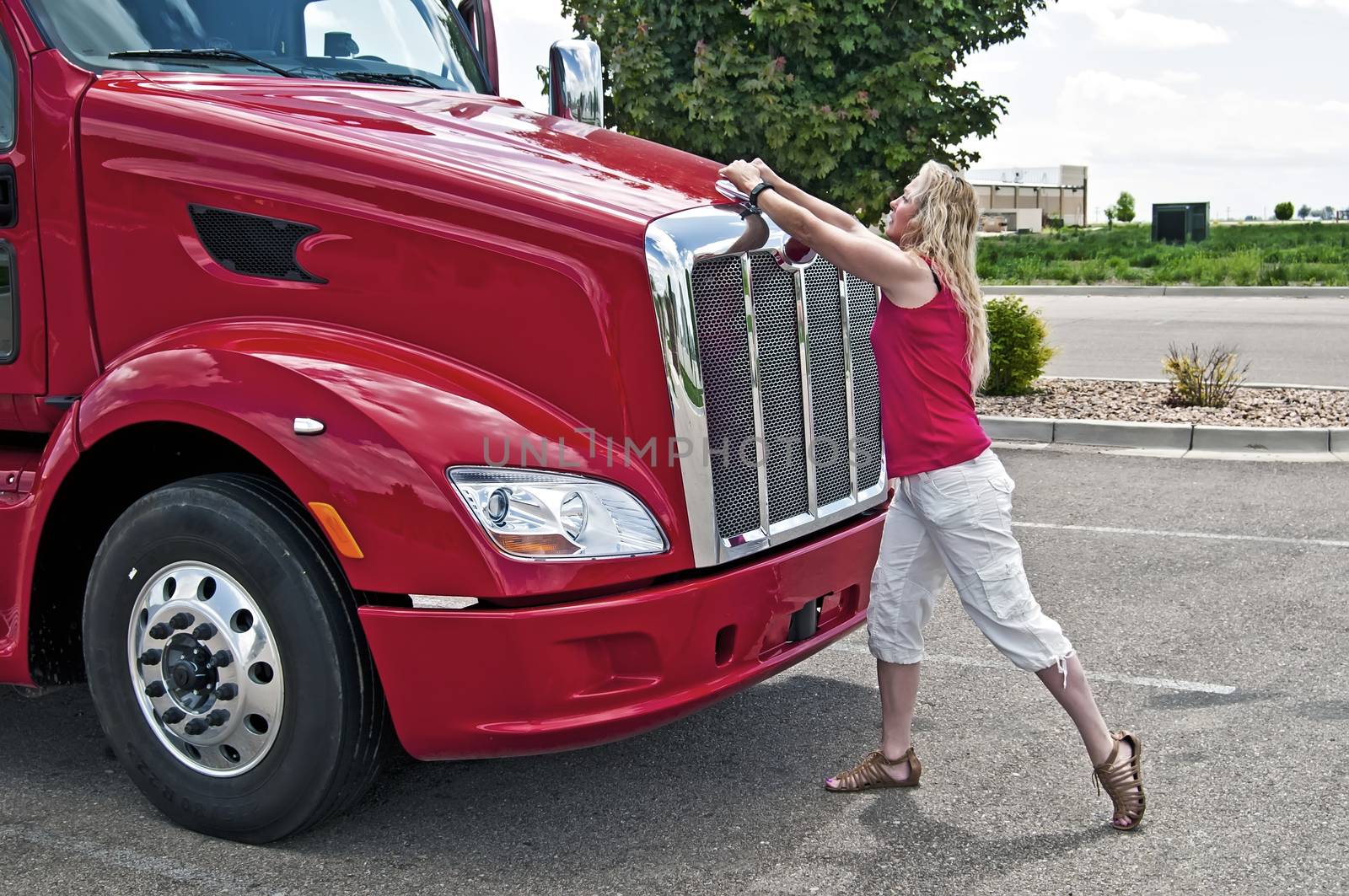 Blonde woman truck driver opening the hood on a semi-truck.