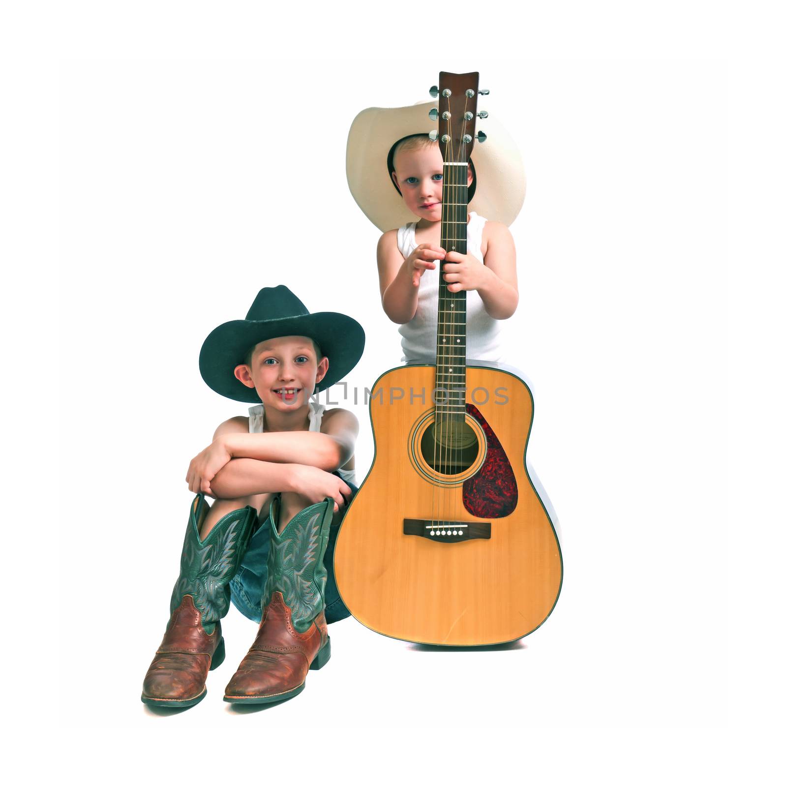 Pre-teen and a pre-schooler with cowboy hats , boots and a guitar, isolated against a white background.