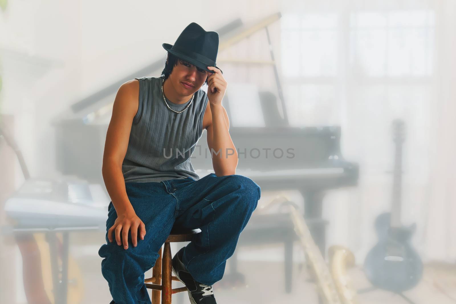 Young blues player resting during a jam session break, sitting on a stool wearing a black fedora.