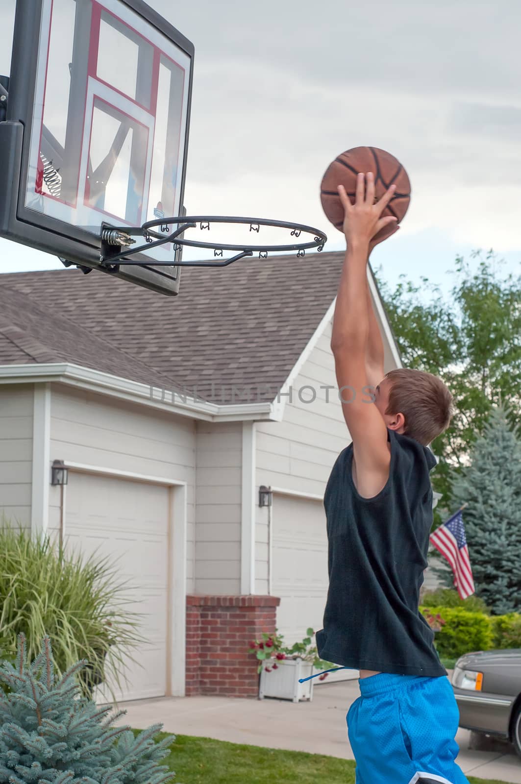 Teenage boy practicing basketball at home on his driveway in a suburban neighborhood.
