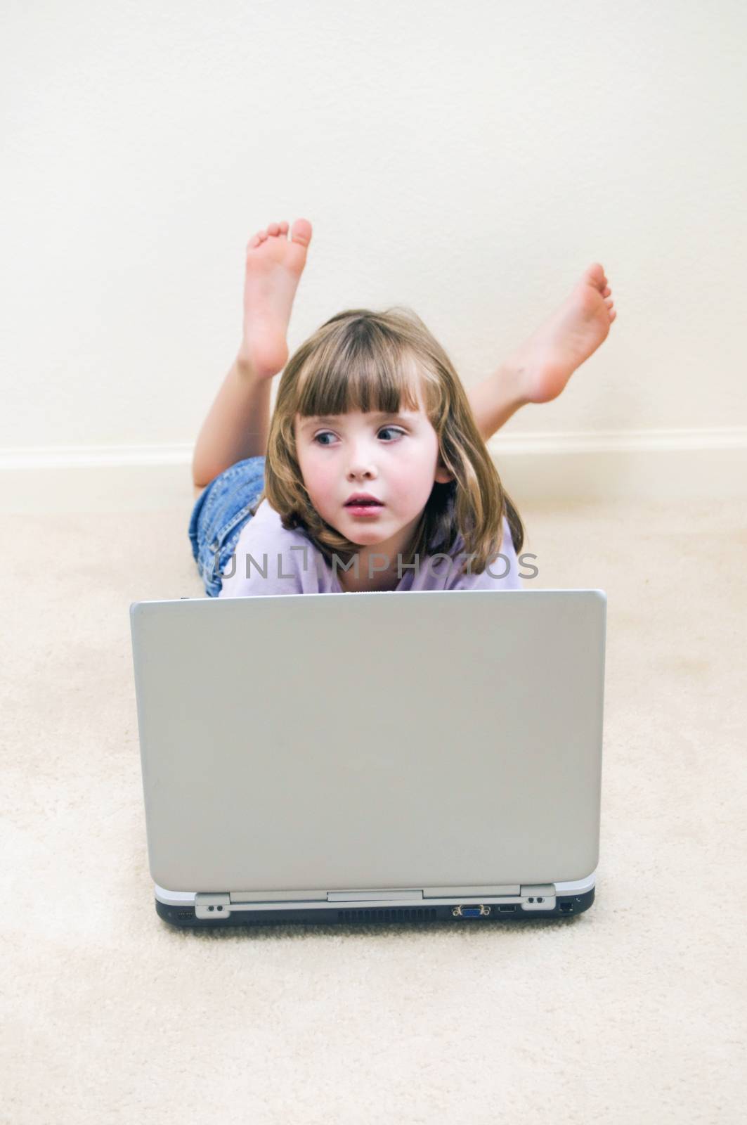 Cute little girl daydreaming while playing on a laptop computer.