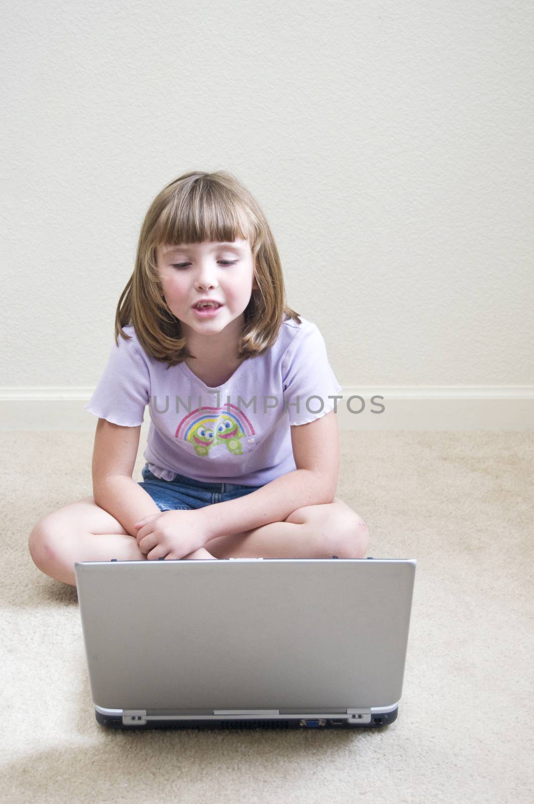 Cute little girl playing a game on a laptop computer while seated on the floor.