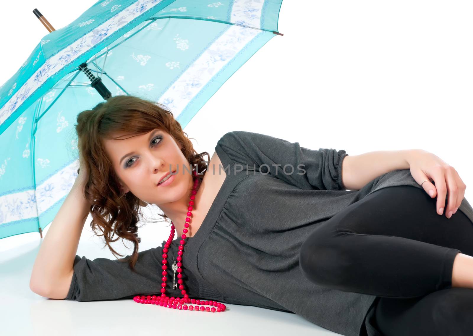 Beautiful young woman reclining under an umbrella against a white background and reflective floor.