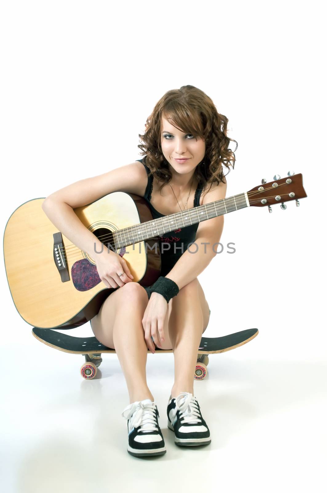 Pretty young woman resting on a scateboard holding a guitar.