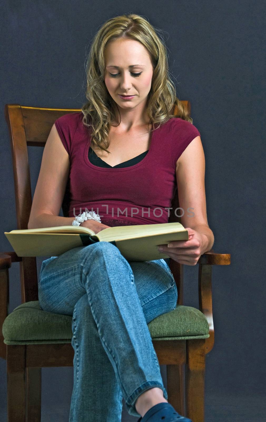 Pretty young lady seated in an arm chair reading a research book.