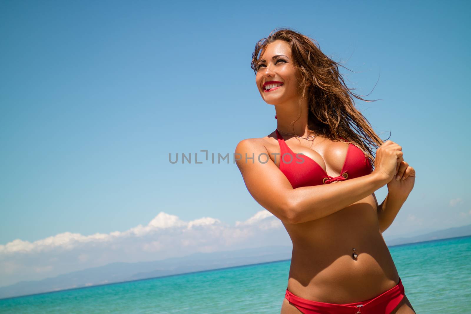 Portrait of a beautiful young woman enjoying on the beach. She is smiling and looking away. 