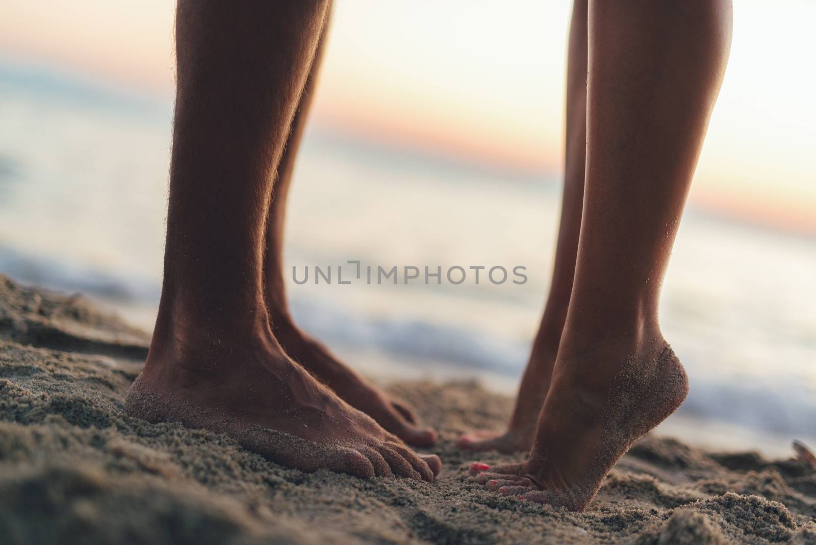 Loving couple hugging and kissing on the sandy beach. Close-up of a couple's feet.