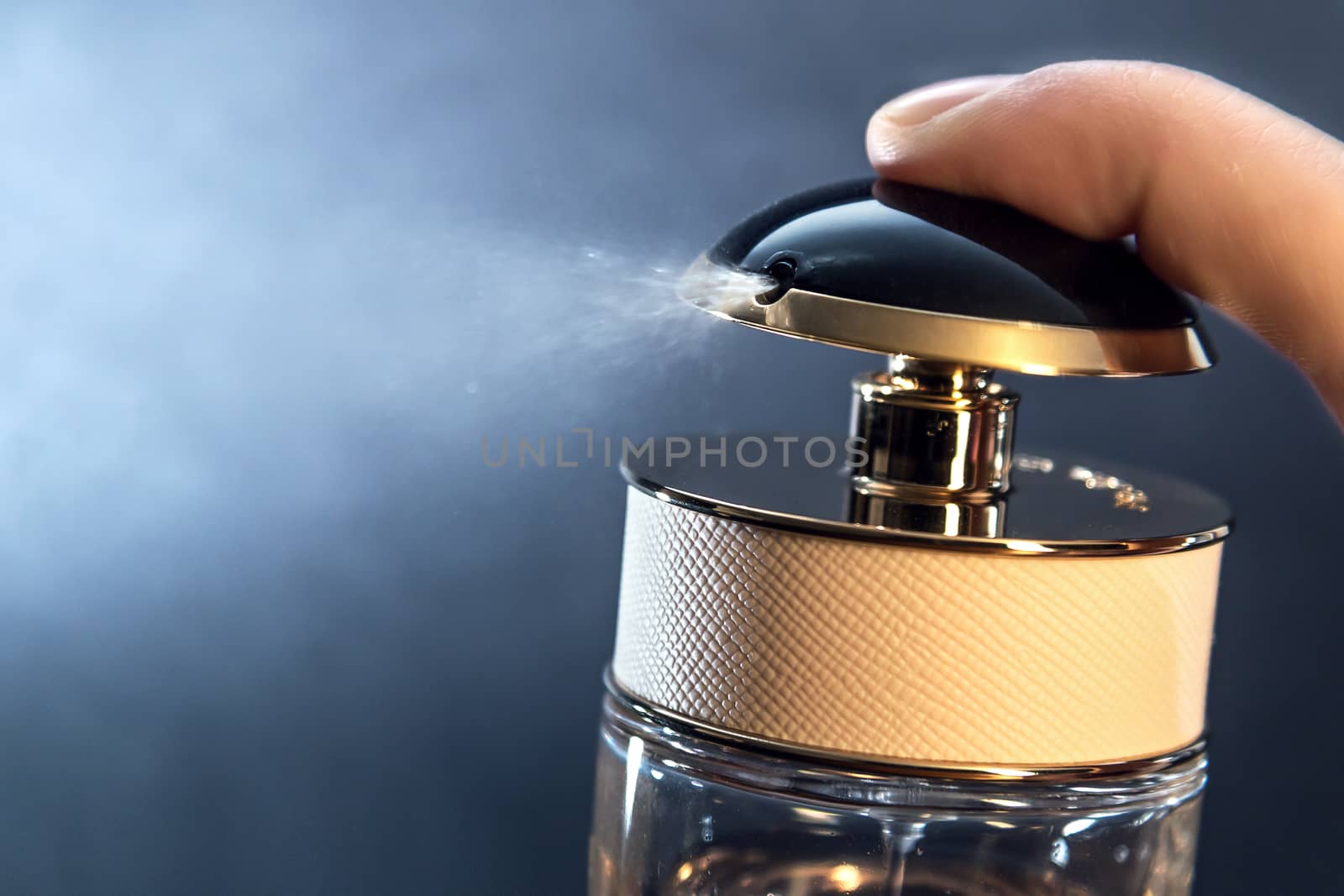 Close up of spraying perfume bottle on a dark grey background