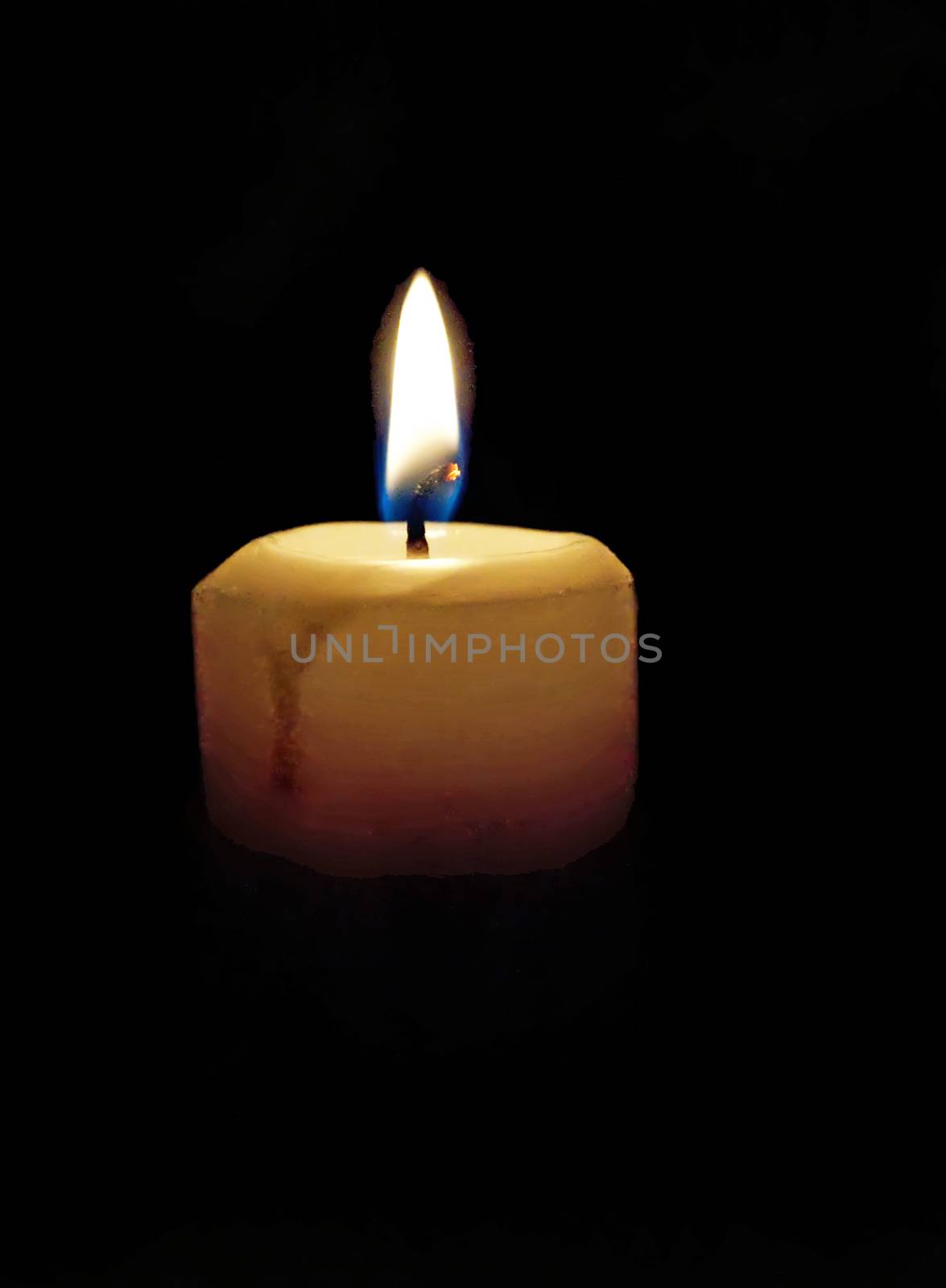 Lighted candle in a darkened room providing a dim light.