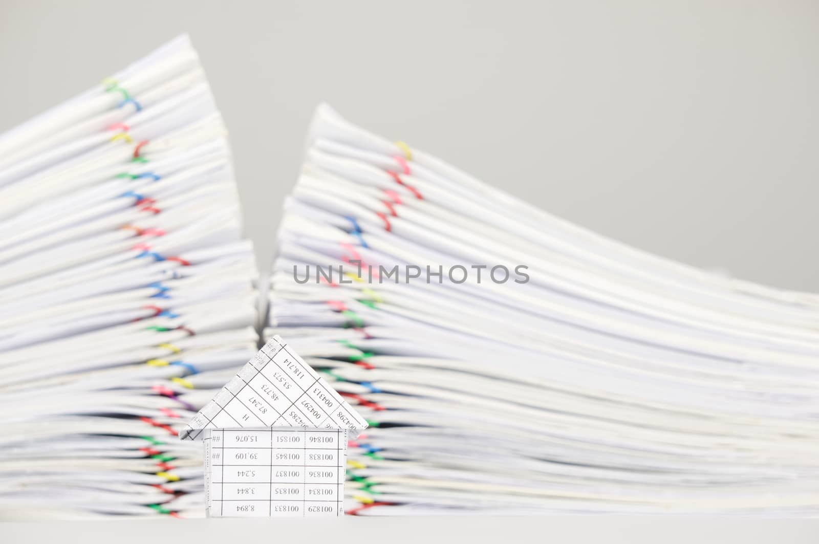 House on white table have blur pile overload of paperwork with colorful paperclip as background.