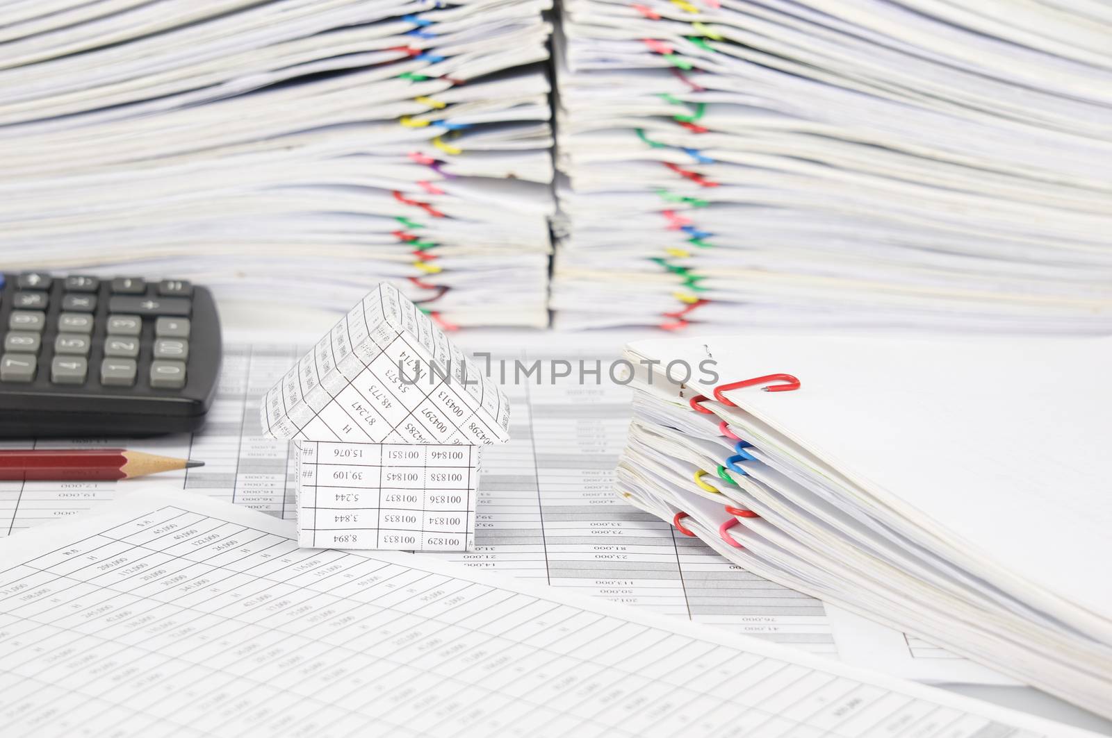 House and pile of document on finance account have blur brown pencil with black calculator and overload of paperwork with colorful paperclip as background.