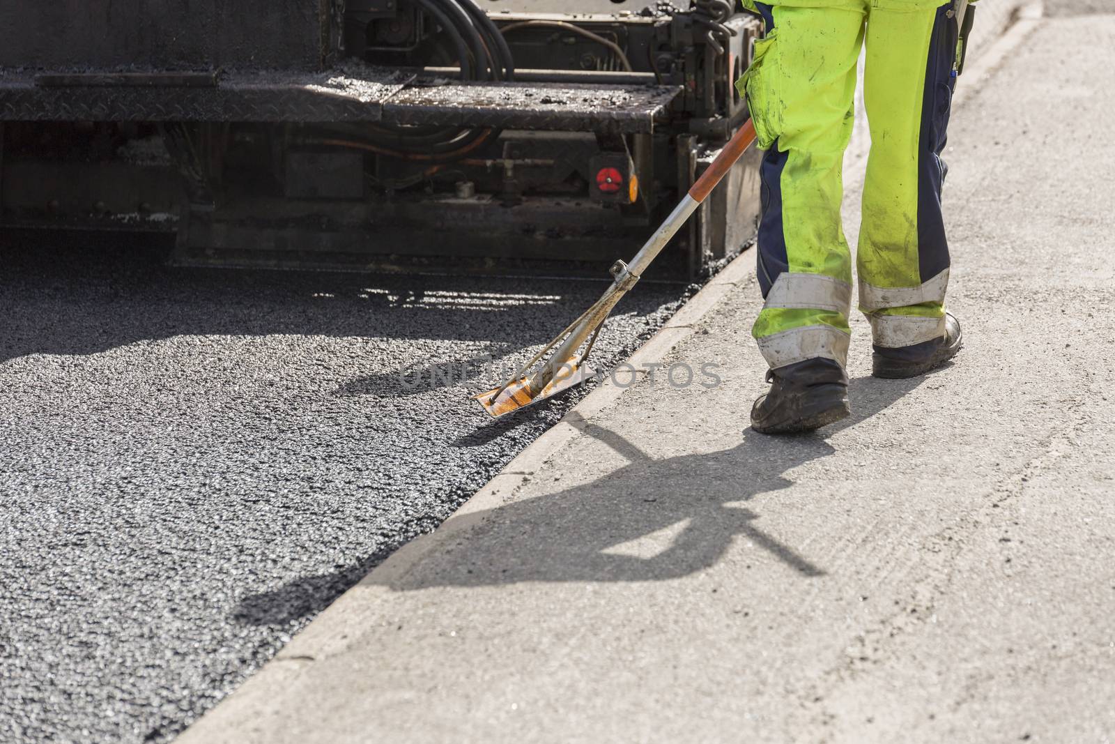 Asphalt Worker Laying Down Asphalt with the paver behind.