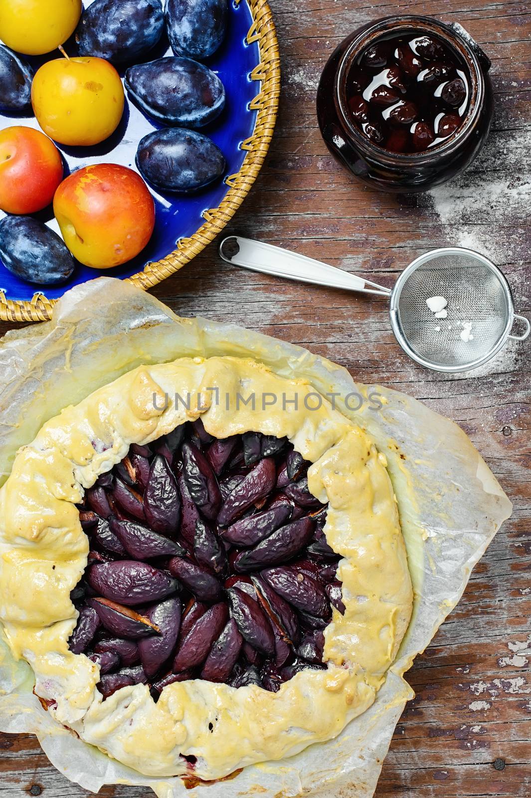 Rustic pie with plums and plum jam on wooden background