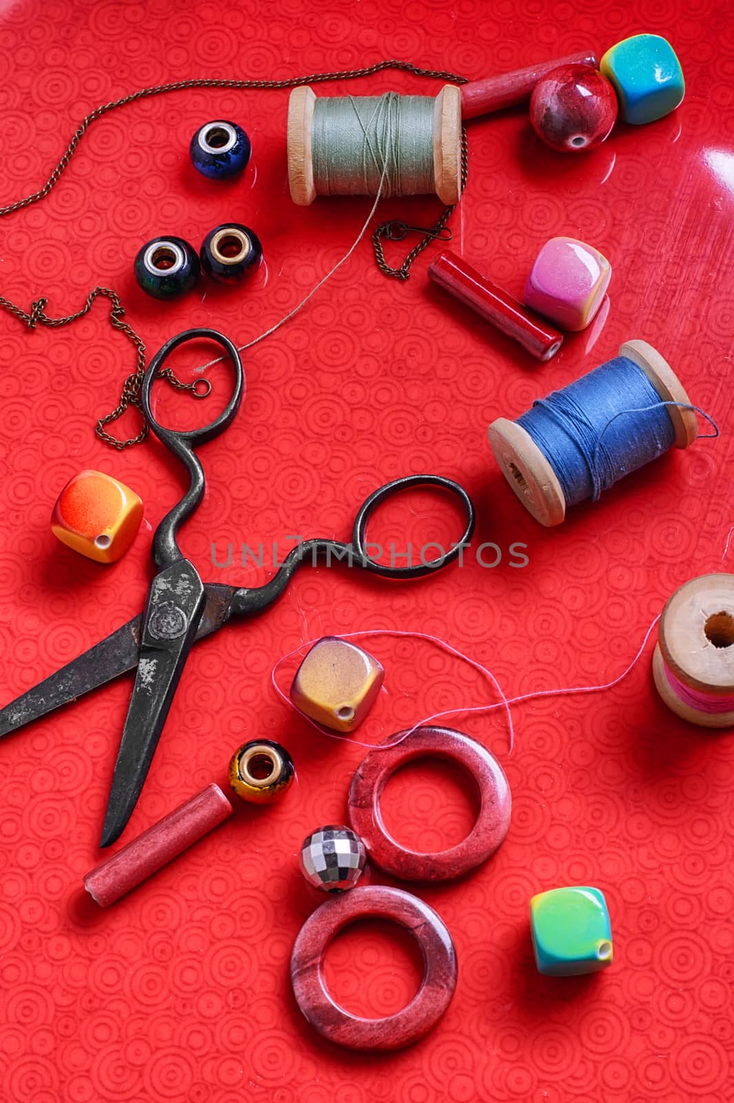 beads for needlework and scissors on bright red background