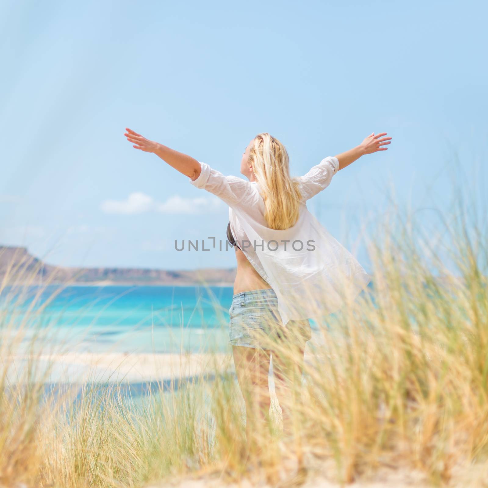 Relaxed woman, arms rised, enjoying sun, freedom and life an a beautiful beach. Young lady feeling free, relaxed and happy. Concept of vacations, freedom, happiness, enjoyment and well being.