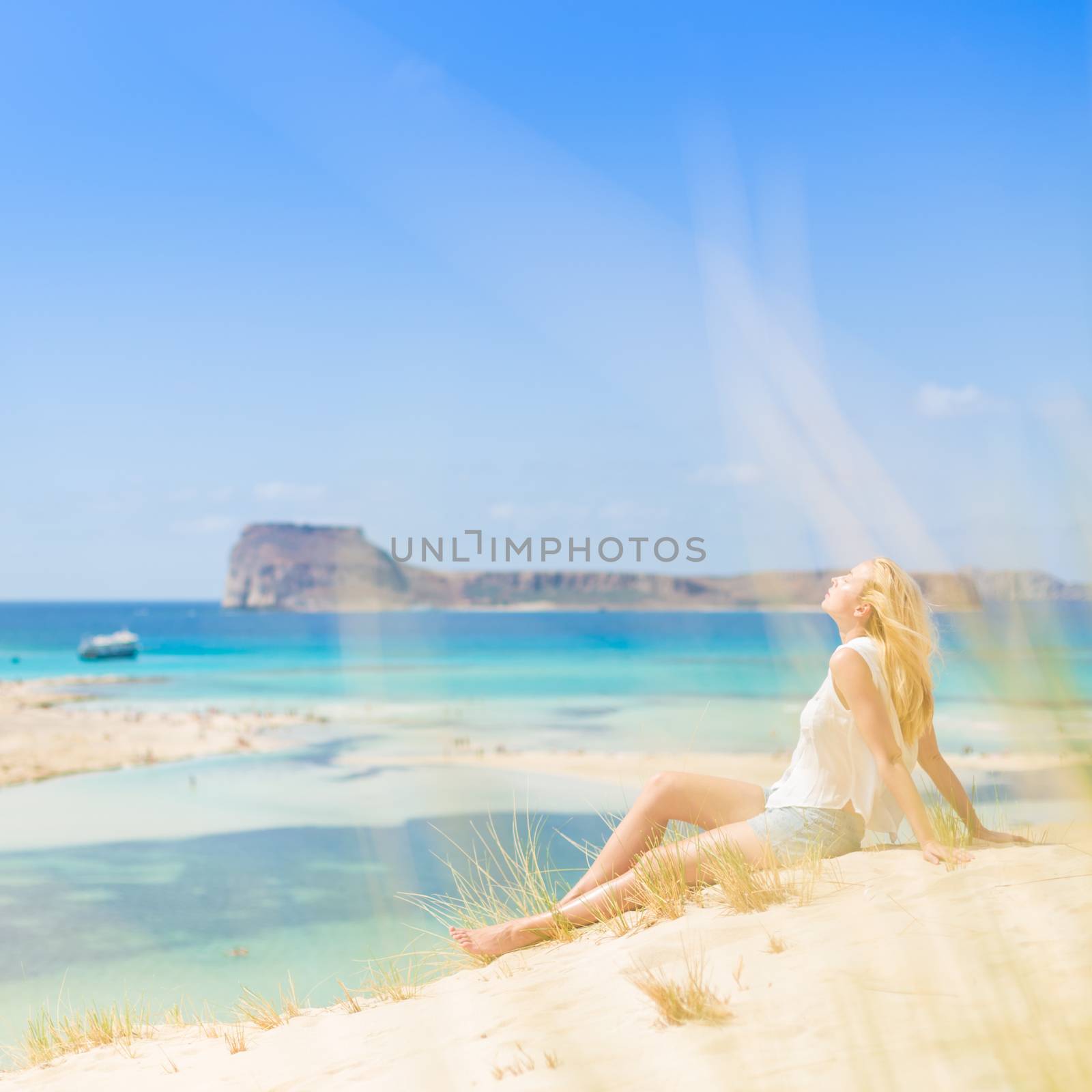 Relaxed woman enjoying sun, freedom and life an a beautiful sandy beach of Balos in Greece. Young lady feeling free, relaxed and happy. Vacations, freedom, happiness, enjoyment and well being.