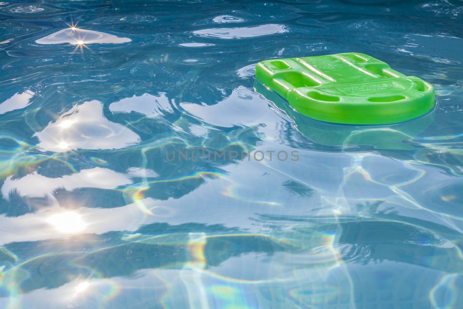 Green lifesaver floating in a swimming pool in summer time with sun reflection