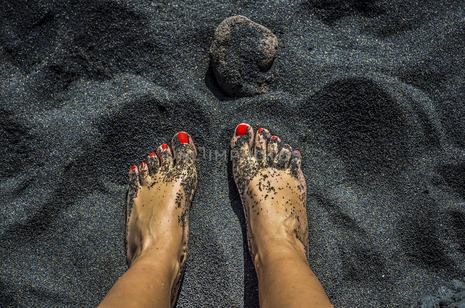 Female bare feet with red nails on black sand beach in Tenerife