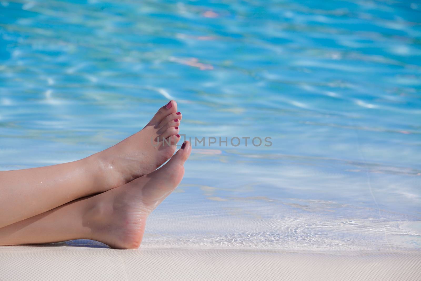 Woman feet on a swimming pool border in summer time