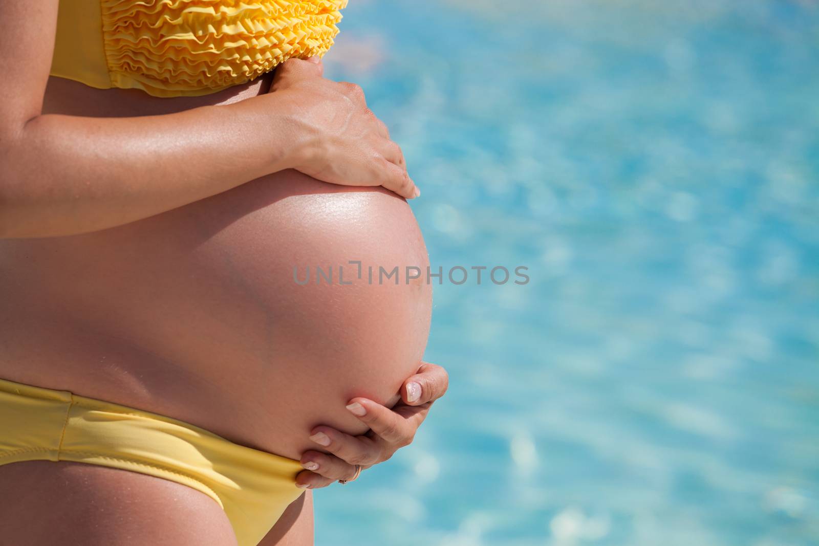 Pregnant woman with hands over tummy in front of a pool