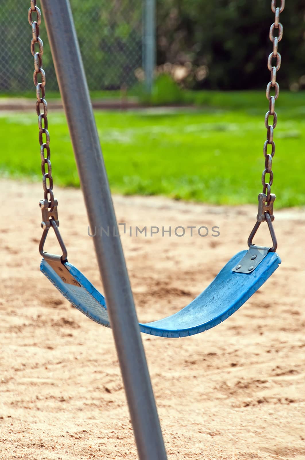 A single park swing sitting idle waiting for joyful children to play on it.