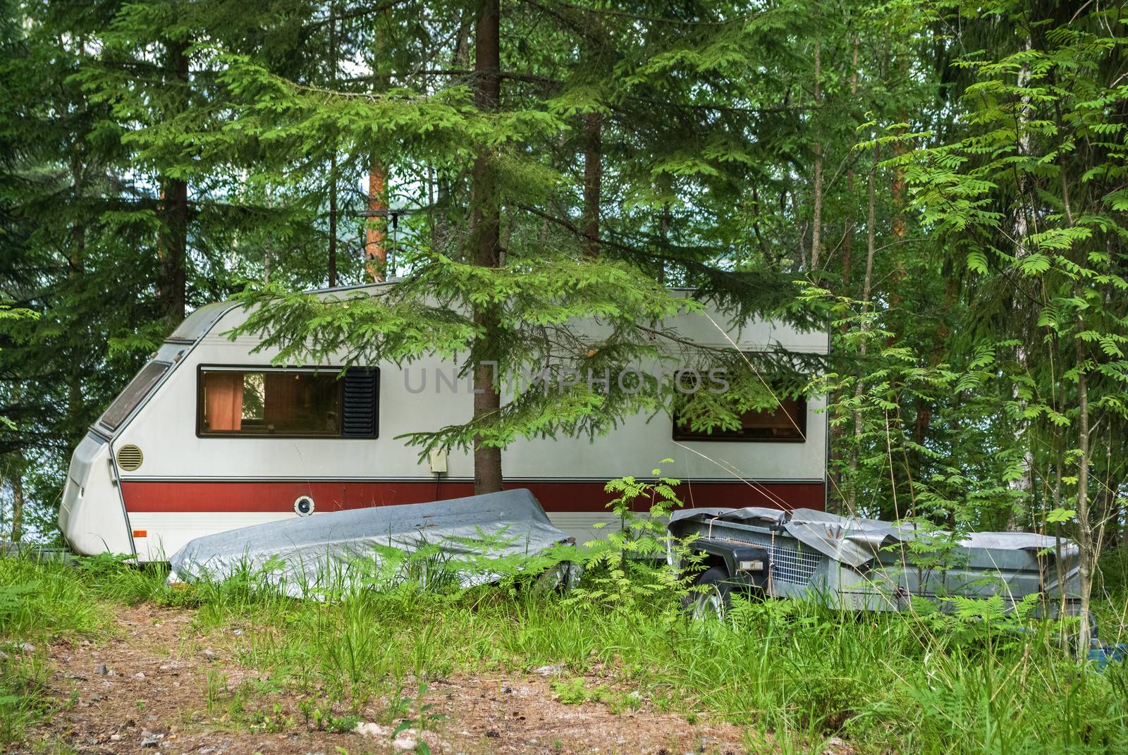 House-trailer parked in the forest, on the lake shore.