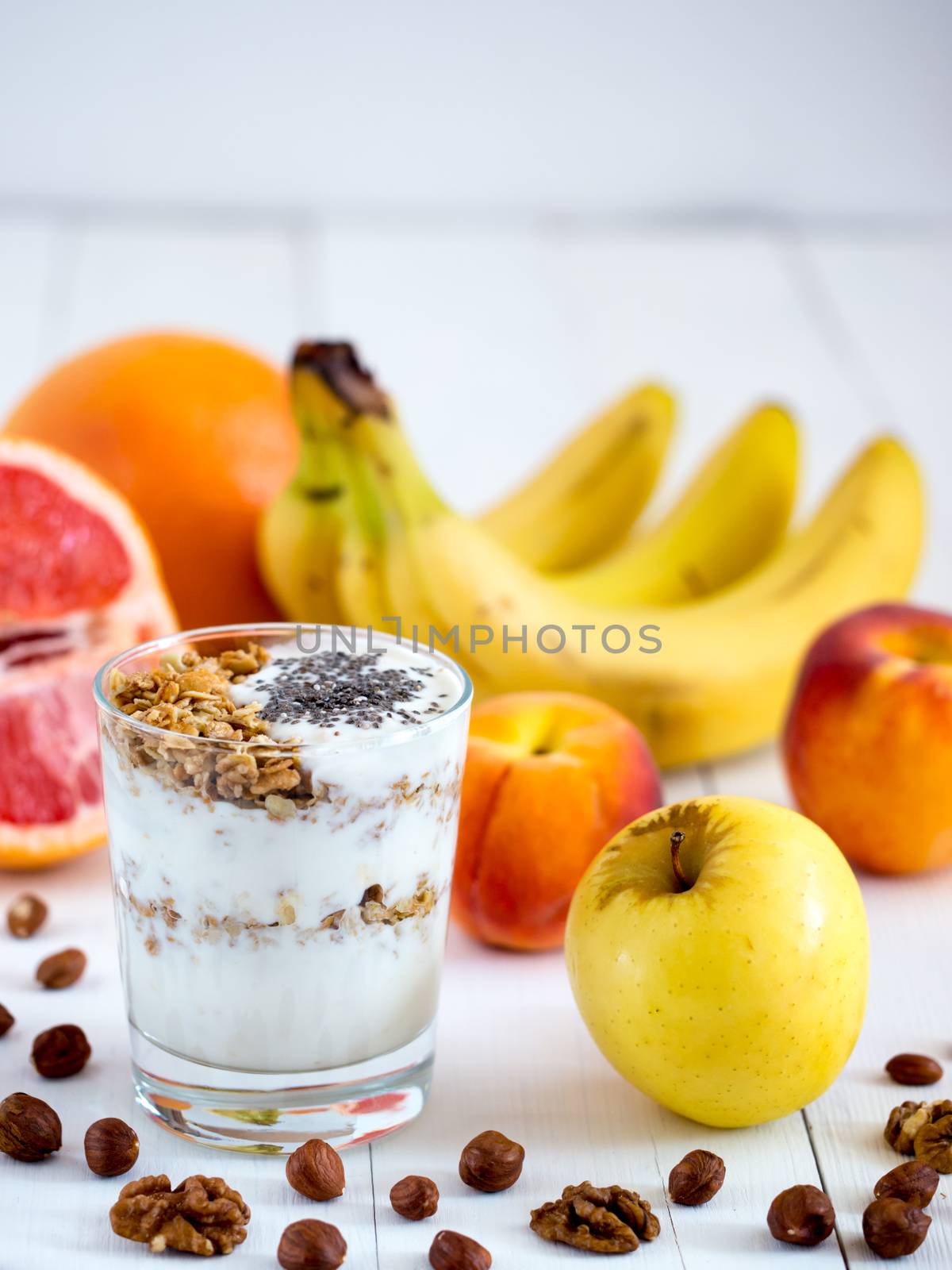 Healthy breakfast: yogurt with muesli and chia seeds, fruits and nuts on white wooden background. Dieting, healthy lifestyle concept meal. Vertical with copyspace
