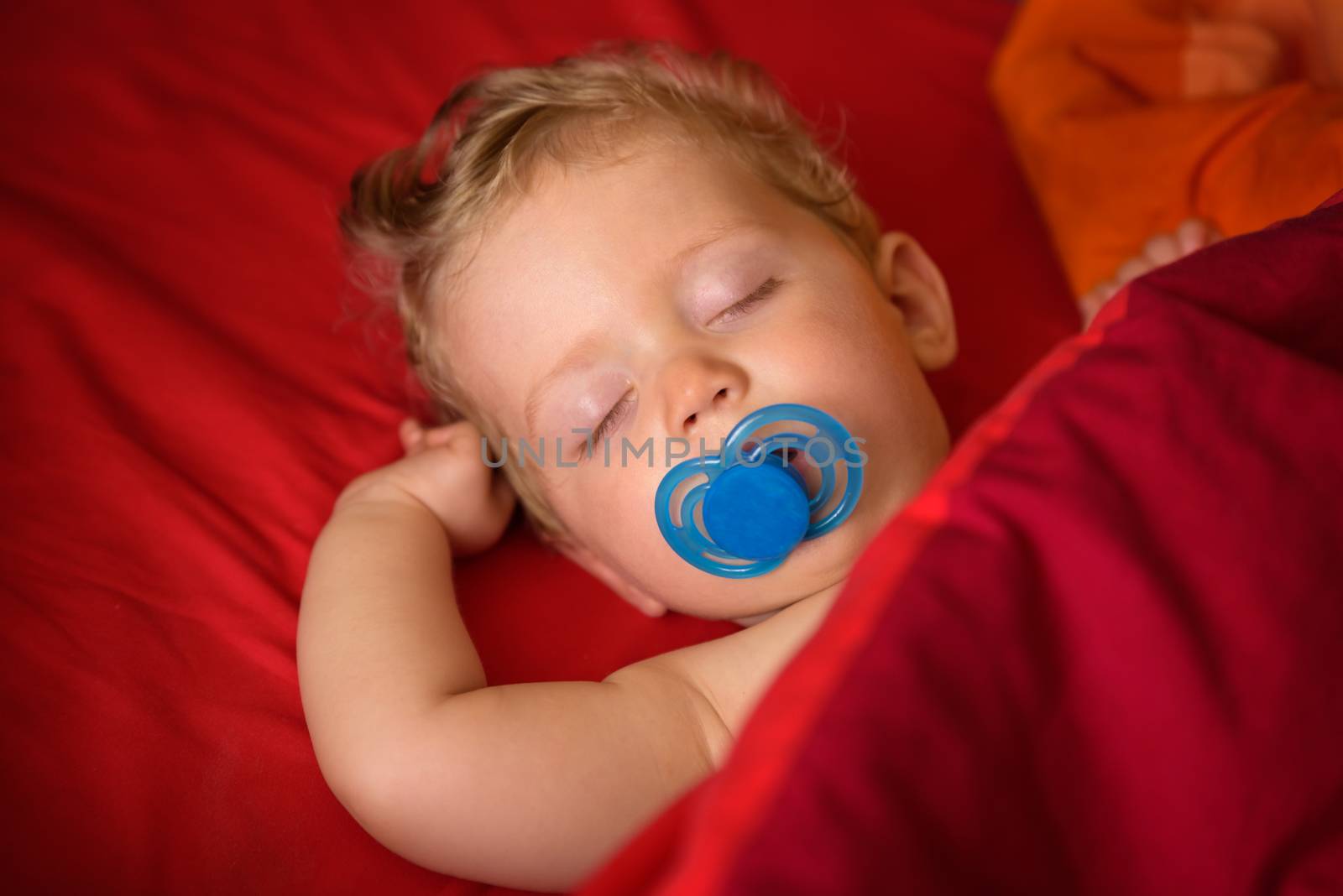 Infant  boy eight month old sleeping with soother in his mouth in red background,close up.