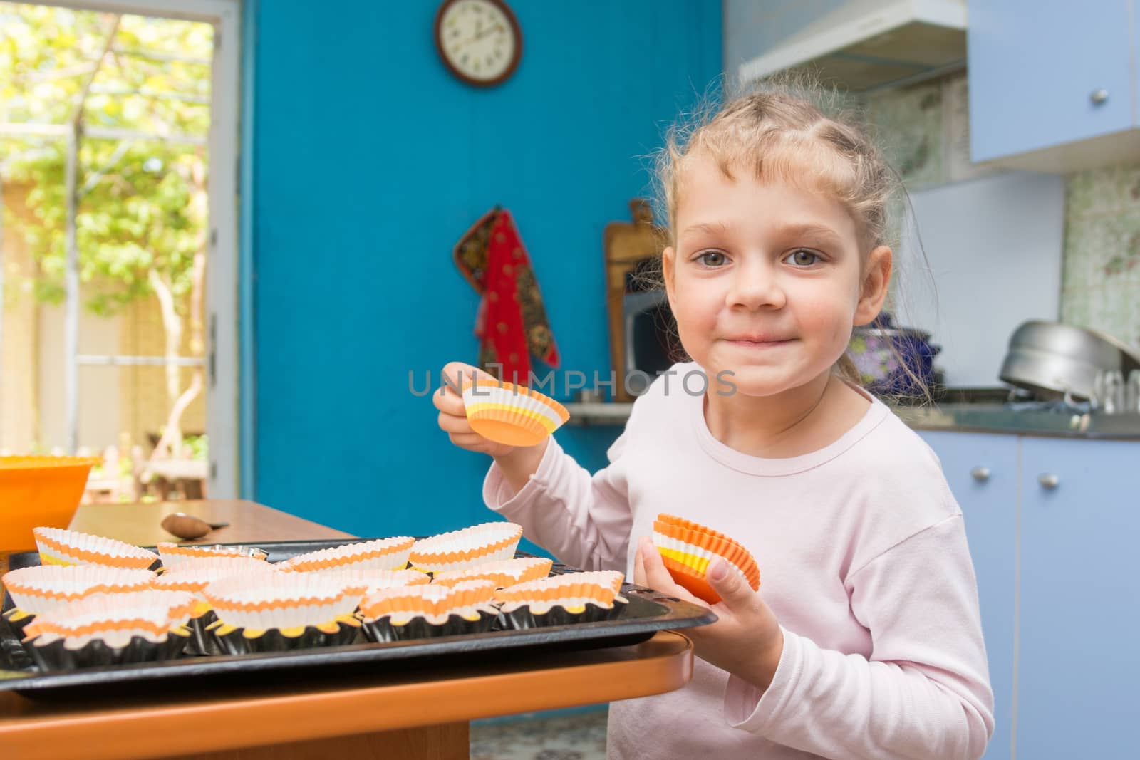 Five-year girl lays on a baking tins Easter cupcakes