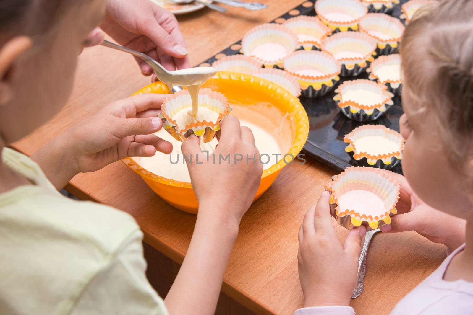 Two girls helped mom to pour batter into the molds for cupcakes by Madhourse